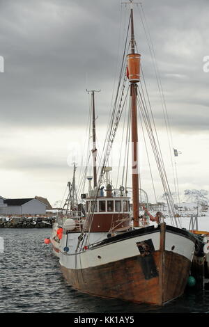 Vecchia barca da pesca con scafo in legno ormeggiata nel porto di pesca tradizionali capanne-rorbuer dipinte di rosso ora per uso turistico-stangerholmen hill in backgroun Foto Stock