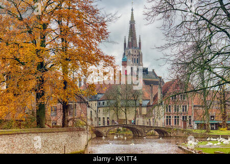 Vista autunnale del beguinage ponte e la chiesa di Nostra Signora torre lungo il canale di Bruges con cigni Foto Stock