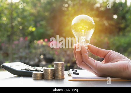 Innovazione o concetto creativo di tenere in mano una lampadina con la calcolatrice. Foto Stock