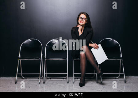 Fiducioso giovane imprenditrice tenendo la carta mentre è seduto su una sedia contro lo sfondo nero Foto Stock