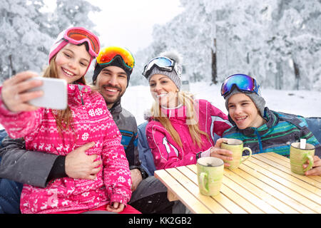 Ragazza rendendo selfie insieme sorridente famiglia in vacanza invernale in montagna Foto Stock