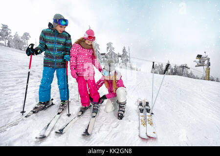 Giovane madre contribuisce alla figlia di correttamente mette scarponi da sci su sci sul terreno di sci Foto Stock