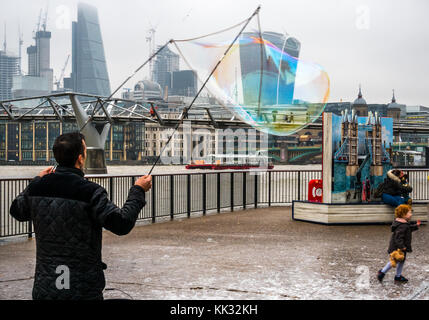 Banca del sud del fiume Tamigi uomo percorso di intrattenimento per bambini e persone con bolle, Londra, Inghilterra, Regno Unito con il Millennium Bridge e pop up Orso Paddington Foto Stock