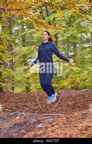 Sporty giovane donna salto con la corda nel parco con colori autunnali sfondo Foto Stock