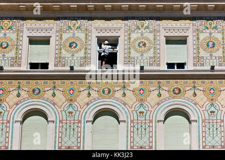 Uomo di lavoro che indossa un'imbracatura, pulisce i vetri dei finestrini. Lavoro pericoloso. Edificio governativo, Piazza dell'unità. Palazzo del Governo.Trieste, Italia, Europa, UE Foto Stock