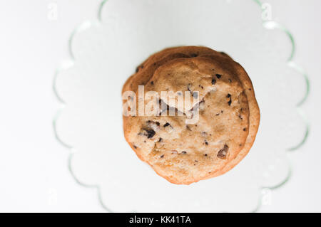 Pila di pane appena sfornato, fatti in casa tradizionale american biscotti con scaglie di cioccolato sulla torta di vetro stand su sfondo bianco Foto Stock