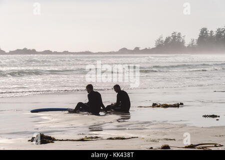 Due surfisti seduti sulla spiaggia di Chesterman vicino a Tofino, BC, Canada (settembre 2017) Foto Stock