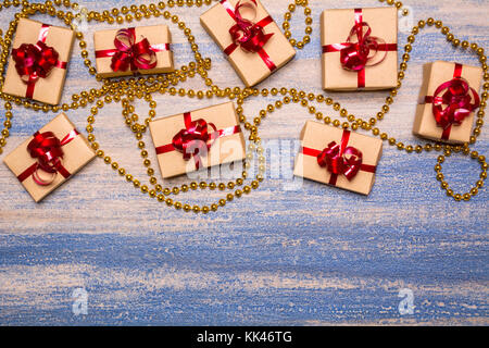 Regali avvolti in carta kraft e legato con un nastro rosso su uno sfondo di legno. sfere d'oro su sfondo blu. festive decorazioni sul tavolo. Foto Stock