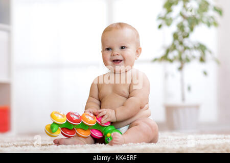 Adorabili poco baby nel pannolino si siede sul tappeto e gioca con il giocattolo a casa. profondità di campo. Foto Stock