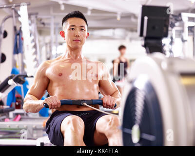 Giovani asiatici Muscolo uomo al lavoro in palestra con vogatore. Foto Stock