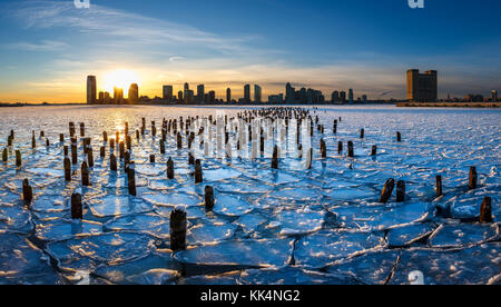 Tramonto sulla congelati Fiume Hudson con il legno vecchio palificazioni e vista sul centro città di Jersey, New Jersey Foto Stock