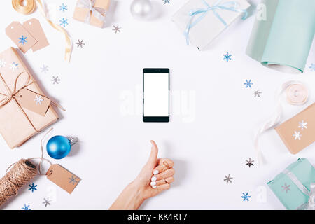 Mani femminili e telefono mobile tra le decorazioni di Natale su un tavolo bianco vista superiore Foto Stock