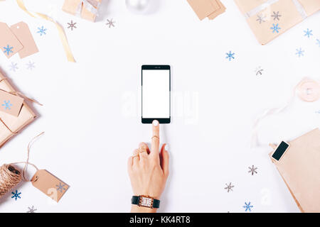 Mani femminili toccando lo schermo di un telefono mobile tra le decorazioni di Natale su un tavolo bianco vista superiore Foto Stock