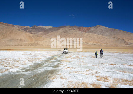 Donna e bambino a piedi da un auto nel paesaggio arido e strati di sale su una limpida giornata autunnale a una fluttuazione di Salt Lake Tso Kar, Ladakh, India Foto Stock