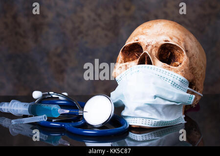 Gruppo di oggetti su un granito, uno stetoscopio , siringa, cranio umano con maschera ,concetto medico Foto Stock