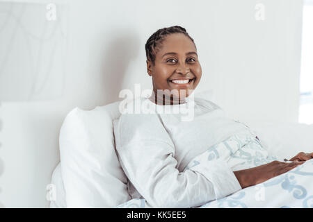 Sorridente giovane donna africana seduta sul suo letto Foto Stock