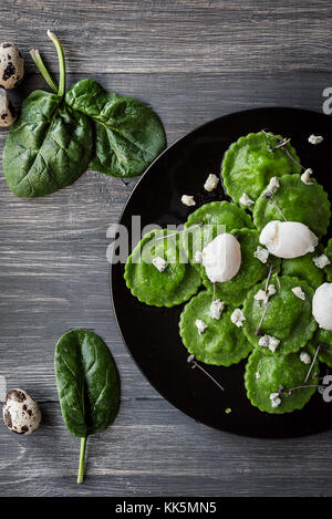 Deliziosi tortelli verdi con l'aggiunta di spinaci, di pasta ripiene di ricotta e funghi porcini. Scottata di uovo di quaglia, formaggio blu. su un nero pla Foto Stock