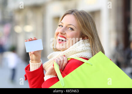 Shopper che mostra un fustellato carta di credito e tenendo le borse della spesa in inverno all'aperto sulla strada Foto Stock