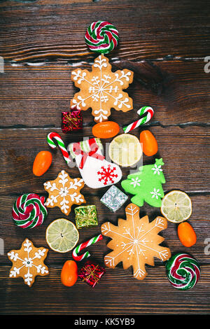 Albero di natale con la caramella da gingerbreads, dolciumi e decori tradizionali su un vecchio legno marrone background. Buon Natale concetto. Foto Stock