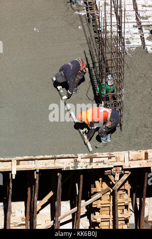 Lavoratori sul sito di costruzione diffusione di calcestruzzo bagnato per rendere il piano di un alto edificio a La Paz in Bolivia Foto Stock