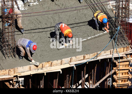 Lavoratori sul sito di costruzione diffusione di calcestruzzo bagnato per rendere il piano di un alto edificio a La Paz in Bolivia Foto Stock