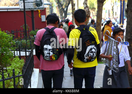 Giovani che indossano zaini con i volti di Jimi Hendrix (L) e Kurt Cobain (R) su di loro che camminano per strada, la Paz, Bolivia Foto Stock