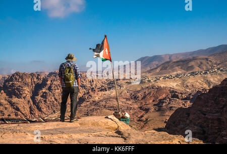 Uomo anziano negli anni '60 in piedi al bordo della scogliera al luogo alto del sacrificio, che domina il sito archeologico di Petra con bandiera giordana, Giordania, Medio Oriente Foto Stock