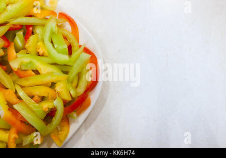 Parte della piastra bianca con fette di strisce longitudinali di ripe multi-peperoni colorati sul vecchio bianco tavola graffiato. Foto Stock