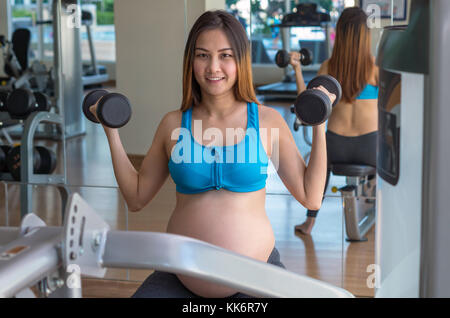 Ritratto di asian femmine gravide di fare esercizio nella sala sportiva, seduto e sollevamento pesi, sana maternità concept Foto Stock