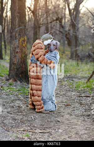 Lunghezza completa di un divertente giovane in amore abbracciando indossando di cane e di gatto costumi di carnevale all'aperto nella foresta Foto Stock