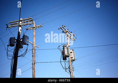 A basso angolo di vista di tre vecchi pali di utilità con cavi e trasformatori per telecomunicazioni ed elettricità contro il cielo blu chiaro con spazio di copia Foto Stock