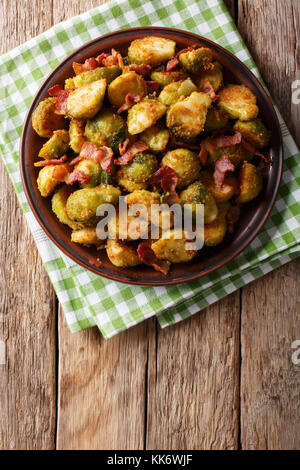 Fritti in panate cavolini di Bruxelles con pancetta close-up su una piastra su una tavola verticale in alto vista da abovel, rustico Foto Stock