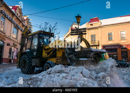 Uzhgorod, Ucraina - 19 gennaio 2017: rimozione della neve sulle strade della città vecchia. persone rimuovere la neve enormi quantità di neve con la guida del trattore con snowp Foto Stock