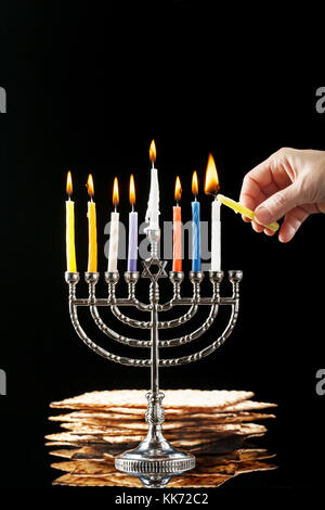 Il menorah con candele accese per hanukkah su uno sfondo nero. matza in background. Foto Stock