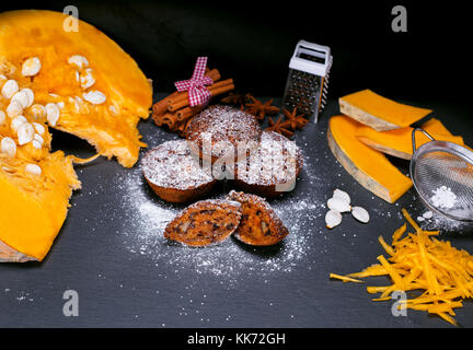 Muffin di zucca e i pezzi di zucca freschi su uno sfondo nero, vista dall'alto Foto Stock