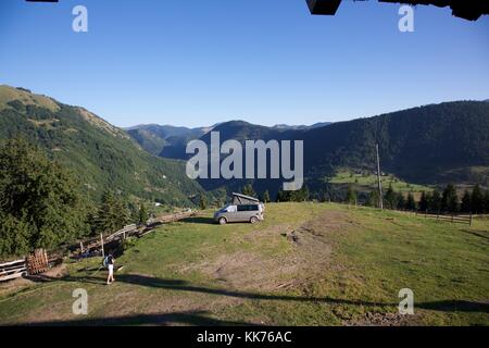 Una femmina di camper di ritornare al suo motorhome in un campo in cima a una collina che domina la valle di Rugova in Kosovo una luminosa giornata di sole. Foto Stock