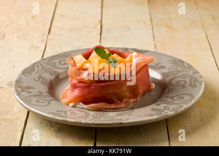 Foto di deliziosa pancetta affettata con melone interno sul tavolo di legno Foto Stock