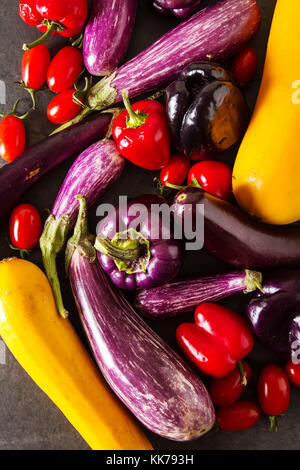 Piccole melanzane, giallo zucchine, pomodori e peperoni viola. sfondo scuro. cibo vegetariano dal villaggio Foto Stock