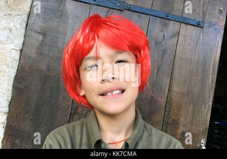 Giovane ragazzo asiatico sorridente con un ritratto rosso parrucca sullo schermo Foto Stock