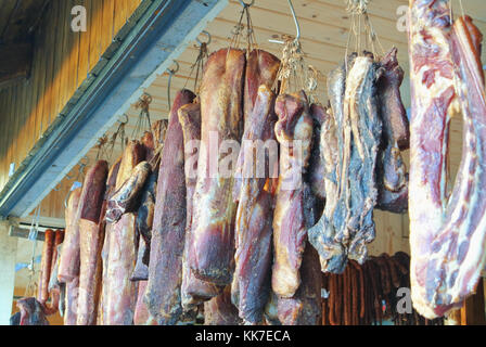 Tradizionale rumena essiccato di maiale affumicato appeso a ganci nel mercato turistico nelle montagne di Romania. Foto Stock