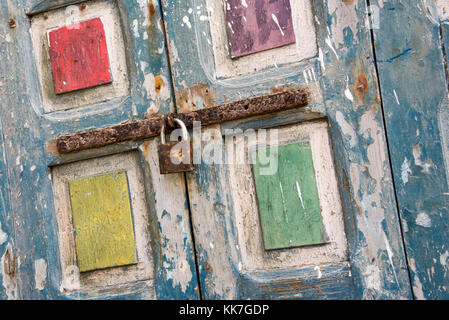 Vivacemente colorato sfaldabile dolore nel blu, giallo, rosso, viola e verde su vecchie persiane alle finestre è fissata con un bullone si arrugginiscano e lucchetto. inclinazione olandese Foto Stock