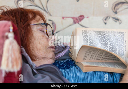 Donna anziana addormentato mentre posa su un divano a leggere un libro. Foto Stock