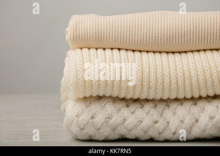 Pila di indumenti a maglia (maglioni, sciarpe, pullover) bianco e beige. messa a fuoco selettiva. Foto Stock