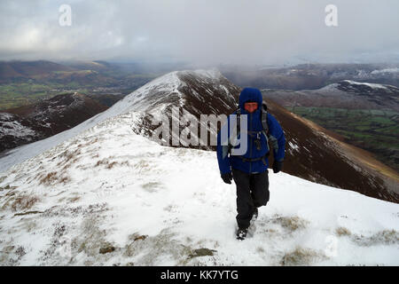 Lone fellwaker maschio su un crinale in direzione wainwright cicatrice dirupi da causey pike nella neve, parco nazionale del distretto dei laghi, cumbria, Regno Unito. Foto Stock