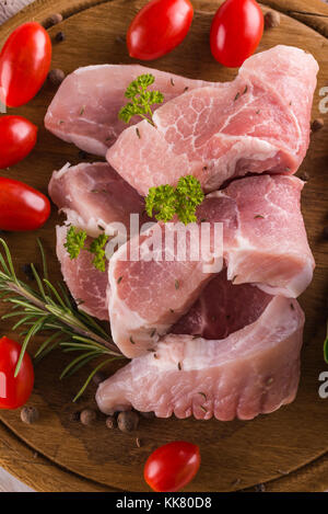 Foto verticale con pochi bistecche di maiale. carne cruda è posto su vintage tavola di legno con pomodori rossi e le erbe aromatiche come il prezzemolo o rosmarino. le fette sono r Foto Stock