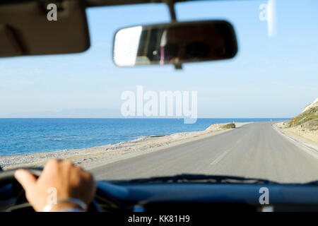 Una vista dall'interno di un automobile come la sua condotta lungo un deserto strada costiera con una spiaggia di sabbia e il mare al lato della strada. Foto Stock