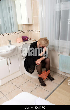 Addolorato donna bionda seduti sul water con le mani sul suo capo Foto Stock