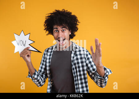 Ritratto di un entusiasta felice l'uomo africano holding wow discorso bolla e guardando la telecamera isolate su sfondo arancione Foto Stock