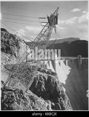 Una fotografia in bianco e nero di una linea di trasmissione a torre e una porzione della Diga di Hoover, la torre fu costruito su una scogliera e supporti angolati verso fuori sopra il canyon, il Lago di Mead e il terreno circostante può essere visto in background, l'immagine proviene da una serie di fotografie noto come il progetto murale di Ansel Adams, fu commissionato dal Servizio del parco nazionale nel 1941 per creare un murale fotografico per il dipartimento dell'interno edificio in Washington DC, il progetto è giunto a termine a causa della Seconda Guerra Mondiale, gli Stati Uniti, 1941. Foto Stock