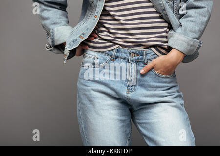 Foto ritagliata della moda femminile in striped tshirt e jeans giacca tenendo in mano la sua tasca, isolata su uno sfondo grigio Foto Stock